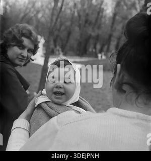 Slawjansk, Ukrainische SSR, Sowjetunion, 1960er Jahre Ein Gruppenporträt, das während eines Spaziergangs im Slaviansk Resort (Slavkurort) Park aufgenommen wurde. Valentina Timofejewna Kravelis (von hinten gesehen) hält ihren lächelnden Sohn Dmitri Michailowitsch Kravelis, der eine weiße Mütze trägt. Links sieht eine Freundin oder Verwandte in dunklem Mantel in die Kamera. Die Gruppe ist von der Natur des Parks umgeben. Dieses Archivfoto fängt einen Moment der Geselligkeit und der Familienurlaub im friedlichen Donbass ein Stockfoto
