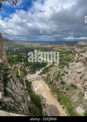 Stunning view of a muddy river flowing through the rocky Rhumel Gorge with an old stone bridge in Constantine. Stockfoto