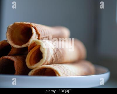 Gerollte Waffelkegel auf einer weißen Platte vor einem neutralen blauen Hintergrund, minimalistisches Food Stillleben. Stockfoto