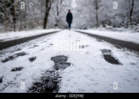 Wintereinbruch im Norden Hude/Oldenburg, Deutschland, 03.01.2026: Eine Person geht auf einer schneebedeckten Straße durch ein Waldgebiet, Fußspuren im Schnee sind im Vordergrund sichtbar. *** Beginn des Winters im Norden Hude Oldenburg, Deutschland 03 01 2026 Eine Person läuft auf einer schneebedeckten Straße durch ein Waldgebiet, Fußspuren im Schnee sind im Vordergrund sichtbar Stockfoto