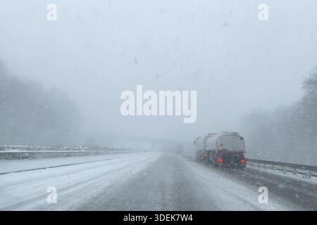 Blick durch die Windschutzscheibe eines Personenkraftwagens bei schlechter Sicht durch leichte Schneefällen auf teilweise überdachten Autobahnen mit sn-Fahrspuren Stockfoto