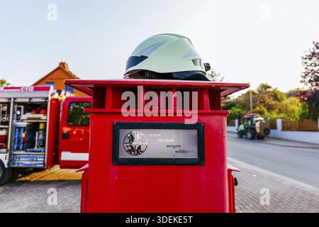 Weißer Helm eines deutschen Feuerwehrmannes auf Feuerwehrmann, Polizei-Notfall-Knopfsäule und Feuerwehrauto vor einer Feuerwache. Retten, bergen, loesche Stockfoto