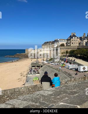 Frankreich. Bretagne. Zitadelle Saint-Malo. Pärchen, die auf den Stadtmauern sitzen und den Strand bei Gebäuden überblicken. Stockfoto