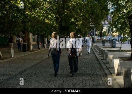 21. September 2025 – Bukarest, Rumänien: Fußgänger spazieren bei Tageslicht auf einer kopfsteingepflasterten, von Bäumen gesäumten Straße im Stadtzentrum. Stockfoto