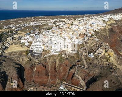 Aus der Vogelperspektive der sonnendurchfluteten weißen Gebäude kaskadieren die zerklüfteten Klippen hinunter zum azurblauen Meer, Oia, Santorin, Griechenland. Stockfoto