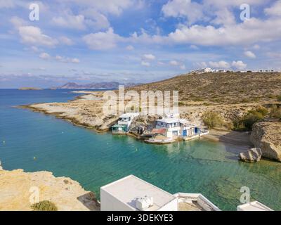 Aus der Vogelperspektive trifft das türkisfarbene Wasser auf die zerklüftete Küste, eingebettet zwischen weißen Gebäuden und der trockenen Landschaft unter hellem Himmel, Milos, Anatoliki A Stockfoto