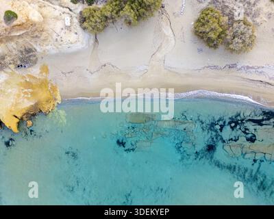 Aus der Vogelperspektive auf das türkisfarbene Meer, das sanft unter der warmen Sonne die Sandküste küsst, im Kontrast zu den zerklüfteten Klippen Milos, Anatoliki Attiki, Greec Stockfoto