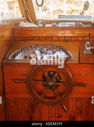 Nahaufnahme eines klassischen hölzernen Schiffsruders in der Kabine des Kapitäns mit poliertem Messinglenkrad, analogen Anzeigen und Hebeln Stockfoto