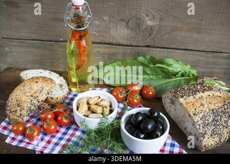 Schwarze Oliven und Muscheln in Keramikschalen, frische Tomaten, Brot und eine Flasche Olivenöl mit Gewürzen auf Holzbrett. Mediterrane Küche auf dunklen woode Stockfoto