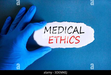 Medizinethik-Symbol. Konzeptworte medizinische Ethik auf wunderschönem Whitepaper. Arzthand in blauem Handschuh. Wunderschöner blauer Hintergrund. Medizinisch gesund Stockfoto