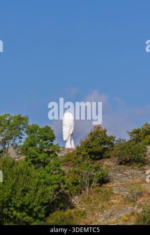 Tjorn, Schweden - 3. September 2025: Ein großer weißer Skulpturenkopf an der Skulptur i Pilane erhebt sich über einem felsigen Hügel, der von Grün umrahmt wird Stockfoto