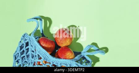 Wiederverwendbare Einkaufstasche, offene Netztasche mit frischen Äpfeln. Blaue Mesh-Einkaufstasche mit Früchten auf grünem Schattenhintergrund. Keine Verschwendung, Eco-Friend Stockfoto