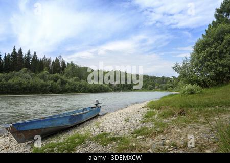 Tagsüber mit einem Bergfluss inmitten von Nadelwäldern mit einem Motorboot an einem felsigen Ufer Stockfoto