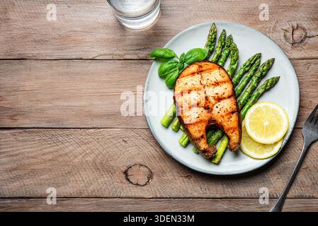 Gegrilltes Lachsfischsteak und gerösteter Spargel auf hölzernem Hintergrund, Blick von oben, Kopierraum. Ausgewogenes Keto-Mittagessen, gesunde Ernährung Konzept. Stockfoto