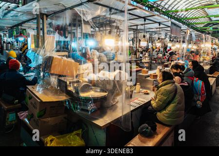 Seoul, 29. Dezember 2024: Käufer essen an einem Lebensmittelstand auf dem Gwangjang Market, der durch Plastikfolien getrennt ist Stockfoto