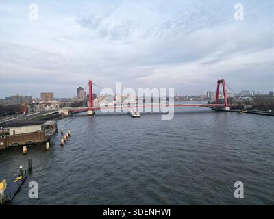 Aus der Vogelperspektive der leuchtend roten Erasmus-Brücke, die sich über den Nieuwe Maas unter bewölktem Himmel erstreckt, Rotterdam, Süd-Holland, Niederlande. Stockfoto