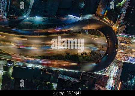 Aus der Vogelperspektive des beleuchteten Überflugs, der sich anmutig durch die Stadt schlängelt, zeichnen Lichtstreifen ein lebendiges Bild vor der dunklen städtischen Dose Stockfoto