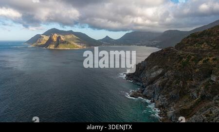Aus der Vogelperspektive sehen Sie das dramatische Zusammentreffen der zerklüfteten Klippen und das weite Meer entlang des Chapmans Peak Drive, einem Tanz aus Licht und Schatten, Kapstadt, Western Cap Stockfoto