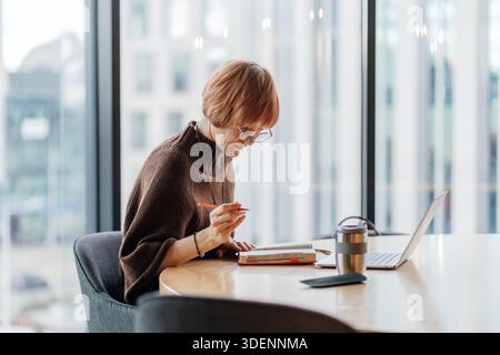 Reife Geschäftsfrau schreibt Notizen am Computer in einem modernen Büro. Stockfoto