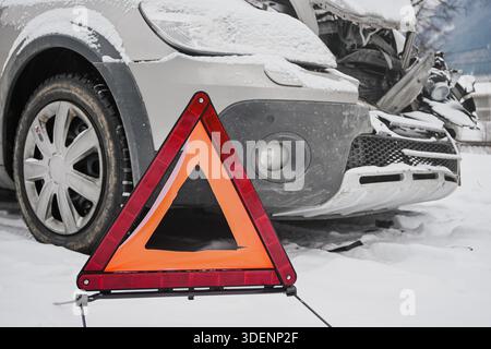Warndreieck vor einem abgestürzten Auto, das im Winter mit Schnee bedeckt ist. Stockfoto