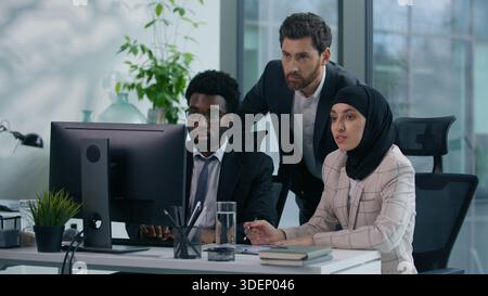 Diverse Unternehmensgruppe diskutiert Projektmarketing-Strategie im Büro mit Blick auf Computerbildschirm afroamerikanischer Mann Frau im Hijab und Kaukasier Stockfoto