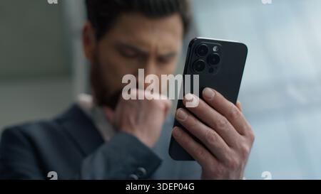 Kaukasischer männlicher Kerl Geschäftsmann Geschäftsmann im Büro, der Smartphone liest schlechte Nachrichten verloren Job Ärger mit Handy aufgebracht frustriert gestresst Stockfoto