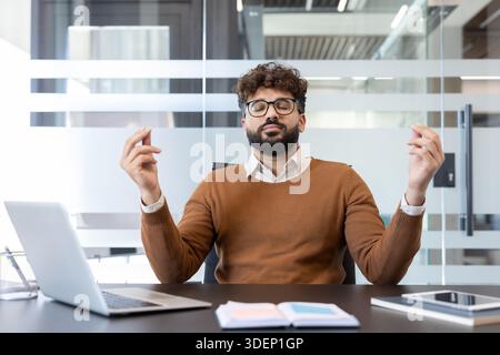 Junger Geschäftsmann, der durch Achtsamkeitsmeditation an seinem modernen Arbeitsplatz Fokus und Entspannung findet, reduziert den Arbeitsstress und verbessert das geistige Wohlbefinden Stockfoto