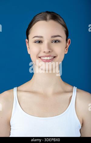 Lächelnde junge Frau mit schöner Haut, die vor blauem Hintergrund Glück findet Stockfoto