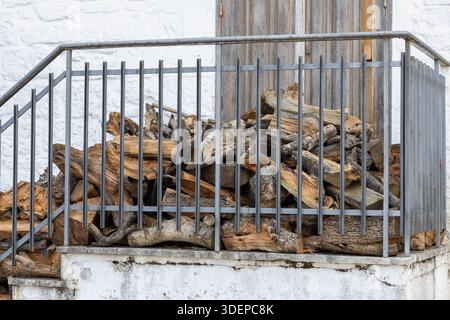 Ein Haufen rustikalen gehackten Brennholzes hinter einem grauen Metallgeländer auf einem weißen Steinbalkon eines traditionellen Hauses in alberobello, italien Stockfoto