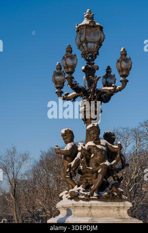 Paris, Frankreich - 01 06 2026: Schneeflocken. Detailansicht der Straßenlaterne und ihrer skulpturalen Cherubs auf der Alexander III Brücke und des Mondes hinter dem sno Stockfoto