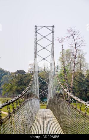 Eine Hängebrücke aus Metall erstreckt sich über eine üppige, baumreiche Naturlandschaft und lädt Wanderer ein, die Wildnis zu erkunden. Stockfoto