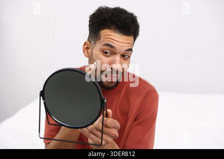 Gutaussehender Mann mit Spiegel, der zu Hause Creme auf sein Gesicht aufträgt Stockfoto