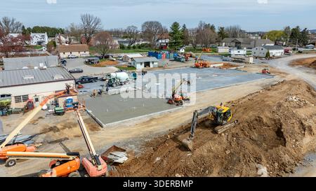 Die Arbeiter sind auf einer Baustelle beschäftigt, auf der Beton gegossen wird. Verschiedene Maschinen sind in Betrieb. Die Szene zeigt einen Entwicklungsbereich mit Häusern und Ausrüstung. Stockfoto