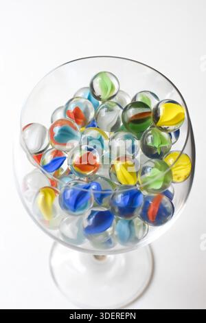 Farbenfrohe Glasmarmor in einer Glasschale auf einem weißen Tisch, Nahaufnahme Stillleben mit verspielter nostalgischer Stimmung und sauberem minimalem Hintergrund. Stockfoto