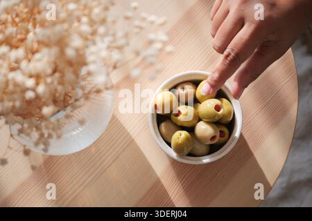 Die Hand greift nach Oliven in einer Schüssel auf einem Holztisch Stockfoto