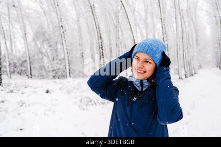 Lächelnde junge Frau genießt Schnee im Wald Stockfoto