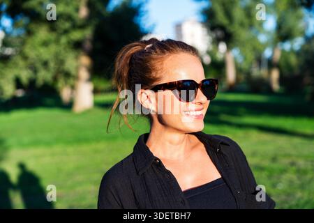 Porträt einer schönen Frau, die eine Sonnenbrille trägt, während sie einen Spaziergang im Freien an sonnigen Tagen genießt. Stockfoto