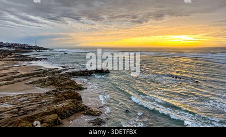 Sonnenuntergang über dem Meer am Asilah Strand, wo die Wellen des Ozeans gegen die Felsen krachen Stockfoto