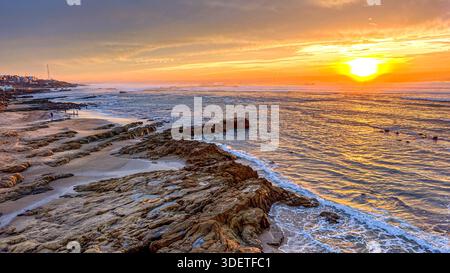 Sonnenuntergang über dem Meer am Asilah Strand, wo die Wellen des Ozeans gegen die Felsen krachen Stockfoto