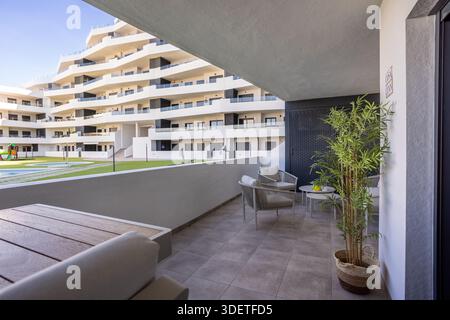Großer überdachter Balkon mit Lounge-Möbeln, Topfpflanzen und Blick auf den modernen Wohnkomplex Stockfoto
