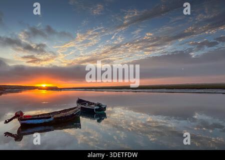Sonnenuntergang über alten hölzernen Fischerbooten, die im ruhigen Wasser der Naila Lagune in Marokko verankert sind. Stockfoto