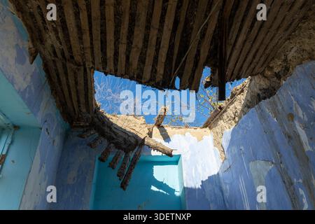 Innenansicht eines alten verlassenen Gebäudes mit einem kaputten Dach, blauen Wänden und klarem Himmel, der durch die beschädigte Decke sichtbar ist. Stockfoto