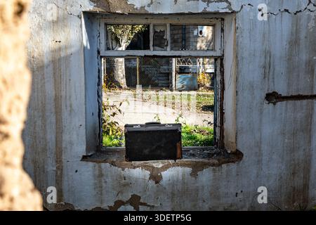 Der Vintage-Koffer befindet sich auf der Fensterbank eines verlassenen Gebäudes, der durch die verwitterten Betonmauern betrachtet wird und an Nostalgie und urbanen Verfall erinnert. Stockfoto