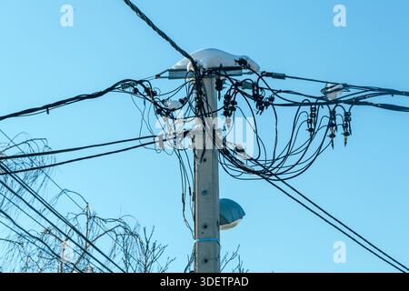 Verwickelte elektrische Leitungen am Versorgungsmast mit Schneekappe im Winter, selektiver Fokus Stockfoto