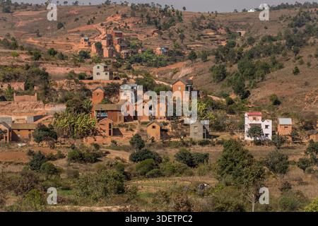 Traditionelle Dorfarchitektur im zentralen Hochland Madagaskars südlich von Antananarivo, nahe Behenjy an der N7. Im zentralen Hochland Madagaskars, insbesondere in den Regionen südlich von Antananarivo, die von den Merina und Betsileo bevölkert werden, besteht die traditionelle Dorfarchitektur oft aus zweistöckigen Häusern mit Dachboden (was sie im Wesentlichen dreistöckig macht), ein Design, das lokal als „Trano Gasy“ („madagassisches Haus“) bekannt ist. Gebrannte rote Tonziegel sind das Standardmaterial, vor allem seit dem 19. Jahrhundert. Die fa-Ade ist oft mit einer Mischung aus Erderde und Zebu-Dung beputzt. Stockfoto