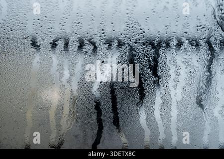 Abstrakte Wassertröpfchen und Kondensationsstreifen an einem kalten Glasfenster. Stockfoto