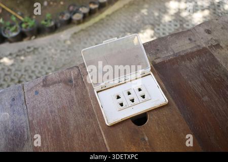 Steckdose für den Außenbereich mit wasserdichter Abdeckung auf Holztisch mit praktischem Zugang zur Stromversorgung für Sicherheit und praktischen Einsatz im Außenbereich Stockfoto