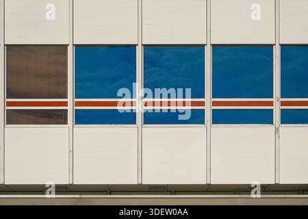 Abschnitt einer modernen Gebäudefassade mit blauen reflektierenden Fenstern und horizontalen roten Streifen in Utrecht, Niederlande. Stockfoto