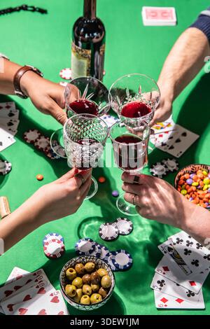 Freunde, die Wein trinken, während sie Poker auf dem grünen Tisch spielen Stockfoto