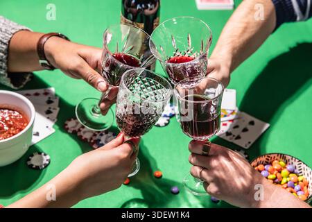 Freunde, die Wein trinken, während sie Poker auf dem grünen Tisch spielen Stockfoto